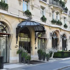 L'elegante ingresso di un edificio parigino, forse sede di Alain Ducasse a Parigi, con lampioni classici e piante verdi.