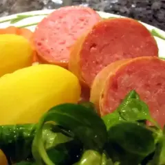 Tranches de saucisson savoureux accompagnées de pommes de terre jaunes et d'une salade verte fraîche.