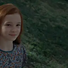 Młoda Lily Evans, przyszła matka Harrego Pottera, z rudymi włosami i w kwiecistej sukience, uśmiecha się na tle zielonego wzgórza.
