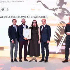 Cztery osoby w garniturach i sukience stoją na scenie, odbierając nagrodę.