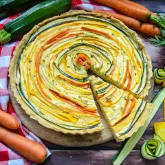 Bunte quiche vegetarisch mit Zucchini und Karotten, kunstvoll im Kreis arrangiert. Daneben frisches Gemüse.