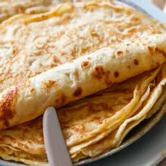 Ein Stapel goldbrauner Eierkuchen, einer davon aufgerollt, liegt auf einem Teller. Ein Messer und eine Gabel liegen daneben. Perfekt für ein einfaches Eierkuchen Rezept.