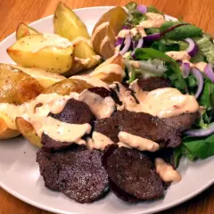 En tallrik med ugnsrostad potatis, saftig kebab och en fräsch sallad med rödlök. En perfekt kebab på plåt för en härlig middag.