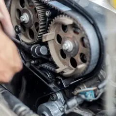 Meccanico lavora sul motore, sostituendo la cinghia di distribuzione. Il costo di questa operazione è importante per la manutenzione.