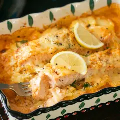 Ein köstlicher Lachs Auflauf mit geschmolzenem Käse und Zitronenscheiben, der gerade mit einer Gabel serviert wird.