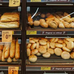 Różne rodzaje pieczywa, w tym bochenki i bułki, na półkach sklepowych.