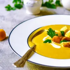 Aksamitna zupa krem z kurek, udekorowana grzankami, świeżą natką pietruszki i szczypiorkiem. Obok talerza leżą świeże kurki.