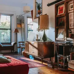 A cozy living room with vintage wood furniture styles, featuring a mid-century dresser, a wooden shelf unit displaying records, and a comfortable armchair.