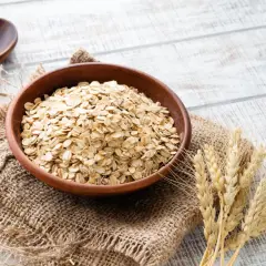 Schüssel mit Haferflocken, die für ihren guten Haferflocken proteingehalt bekannt sind, daneben eine Holzschale und Weizenähren.