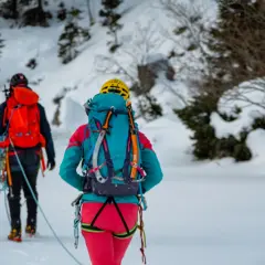 Dwóch alpinistów w zimowych górach, z plecakami i linami. Wiedzą, co zabrać w góry zimą: kask, raki, czekany i ciepłą odzież.