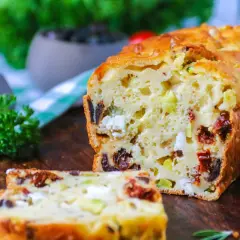 Un délicieux cake salé aux olives, tomates séchées et feta, coupé en tranches sur une planche en bois.