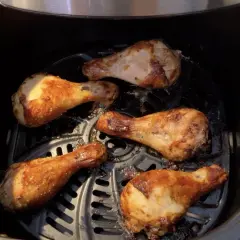 Cinq pilons de poulet dorés et croustillants cuisent dans une friteuse à air.