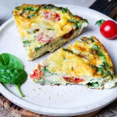 Zwei Stücke einer herzhaften Frittata mit Spinat und Tomaten auf einem Teller, garniert mit frischen Spinatblättern und Kirschtomaten. Ein köstliches Frittata Rezept.