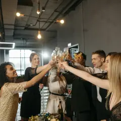 Grupa ludzi w eleganckich strojach na uroczystą kolację firmową wznosi toasty szampanem.