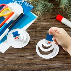 Niño crea muñecos de nieve con manualidades de invierno. Tijeras, rotuladores y pegamento listos para la diversión.