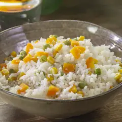 Un tazón de arroz blanco con trozos de zanahoria, guisantes y maíz. Un plato sencillo y delicioso de arroz con verduras salteadas.