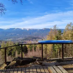 Widok z punktu widokowego na góry, las i miasteczko. Na pierwszym planie drewniany taras i balustrada. W oddali majaczy zakręt śmierci.