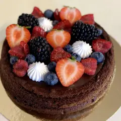 En mörk chokladtårta med ganache, toppad med färska bär och maränger. En festlig chokladtårta med ganache som ser utsökt ut.