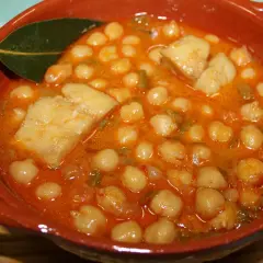 Garbanzos con bacalao, la receta de la abuela, servidos en cazuela de barro con hoja de laurel.