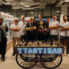 Grupa osób pozuje przy stoisku TTARTISAN z obiektywami.