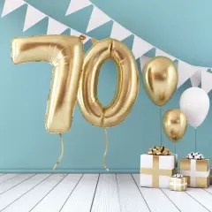Złote balony z cyfrą 70 i prezenty tworzą piękną scenografię na życzenia na 70 urodziny.