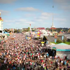 Tłum ludzi na festynie, widoczny wieżowiec z wielkim kuflem piwa i karuzele. To prawdziwy Oktoberfest!