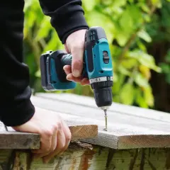 Main tenant une perceuse sans fil, il visse une planche de bois. La puissance perceuse permet de réaliser des travaux de bricolage facilement.