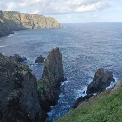 Acantilados escarpados y rocas emergiendo del mar azul en la **costa Artabra**. El cielo nublado ilumina el paisaje salvaje.