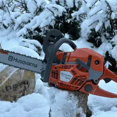 Pomarańczowa piła łańcuchowa Husqvarna 560 XP na tle zaśnieżonych drzew. Poznaj husqvarna 560 xp dane techniczne.