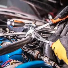Mechanik w rękawiczkach naprawia układ hamulcowy samochodu, używając klucza nastawnego i grzechotki.