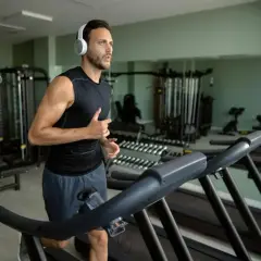 Mężczyzna w słuchawkach biegnie na bieżni, wykonując trening cardio na siłowni.
