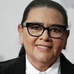 María del Monte, con gafas negras y una sonrisa amable, luce un traje elegante.