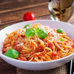 Un piatto di spaghetti alla corte d'assise, conditi con pomodoro fresco e basilico, spolverati di parmigiano.