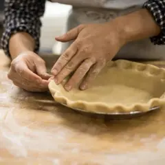 Mains farinées façonnant une pâte à tarte dans un moule. L'ajout d'une touche d'ammonium bicarbonate assure une croûte légère et croustillante.
