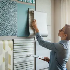 En person väljer tapet. Hon håller upp en rulle med en randig non woven-tapet som betyder att den är lätt att sätta upp.