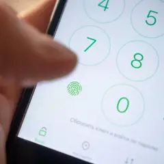 Zbliżenie na ekran telefonu z klawiaturą numeryczną, ikoną odcisku palca i palcem wskazującym.