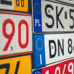 Zbliżenie na stos tablic rejestracyjnych z kodami krajów UE, w tym PL, SK i DN.