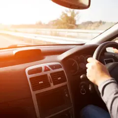 Widok z wnętrza samochodu, ręce na kierownicy, słońce.