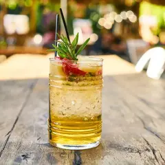 Orzeźwiający drink z sokiem ananasowym, lodem i owocami, ozdobiony gałązką rozmarynu, na drewnianym stole.