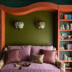 A cozy reading nook with a pink sofa, shelves filled with books and decor, and bright bold colors on the walls and shelving.