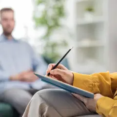 Terapeuta notuje podczas sesji. Mężczyzna siedzi na kanapie, słuchając uważnie. f 60.8.
