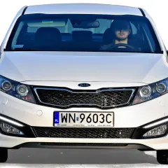 Białe auto z Korei Południowej, model Kia, z młodym kierowcą za kierownicą.