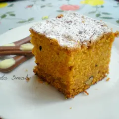 Pyszne ciasto marchewkowe z dużej blachy, posypane cukrem pudrem, na talerzu z czekoladowymi paluszkami.