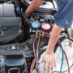 Mecánico realizando la tarea de cargar gas aire acondicionado en un coche, con manómetros y mangueras conectadas al motor.