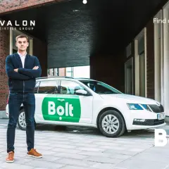 Młody mężczyzna stoi obok białego samochodu z logo Bolt. Zastanawiasz się, ile można zarobić na Bolcie?