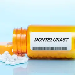 Pomarańczowa buteleczka z lekami, na której widnieje napis MONTELUKAST. Obok rozsypane białe tabletki.