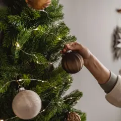 Eine Hand schmückt einen Wand-Weihnachtsbaum mit Kugeln und Lichterkette. So kann man einen Weihnachtsbaum selber machen, auch ohne Platz.