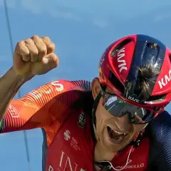 Michał Kwiatkowski, kolarz, triumfuje z zaciśniętą pięścią na tle błękitnego nieba.