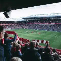 Kibice na stadionie, z szalikami w dłoniach, czekają na wznowienie gry. Zastanawiają się, ile trwa przerwa w meczu.