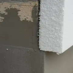 Fragment ściany z nałożonym tynkiem i siatką, obok biały styrobeton.